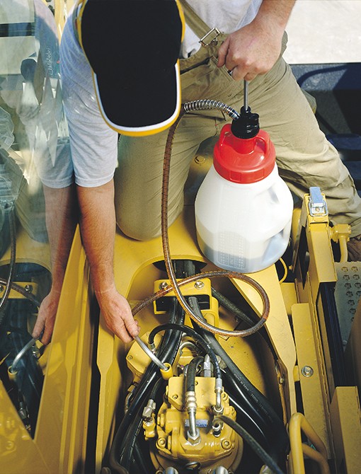 FluidManagement a middle aged man pours lubricant from a transfer container into an industrial machine.
